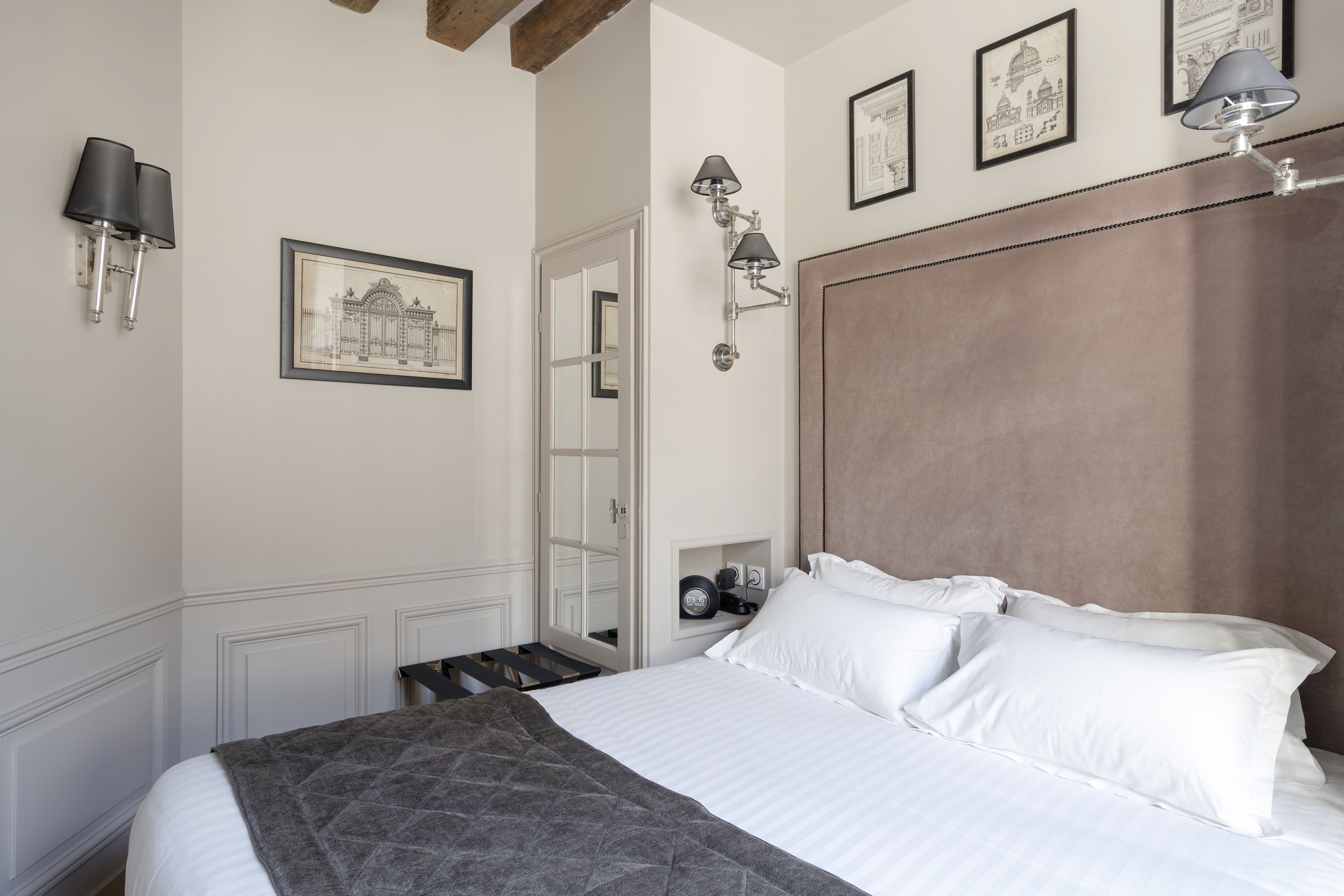 A neatly made bed with white linens and a gray throw blanket, a wooden headboard, and wall-mounted lamps.