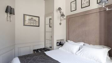 A neatly made bed with white linens and a gray throw blanket, a wooden headboard, and wall-mounted lamps.