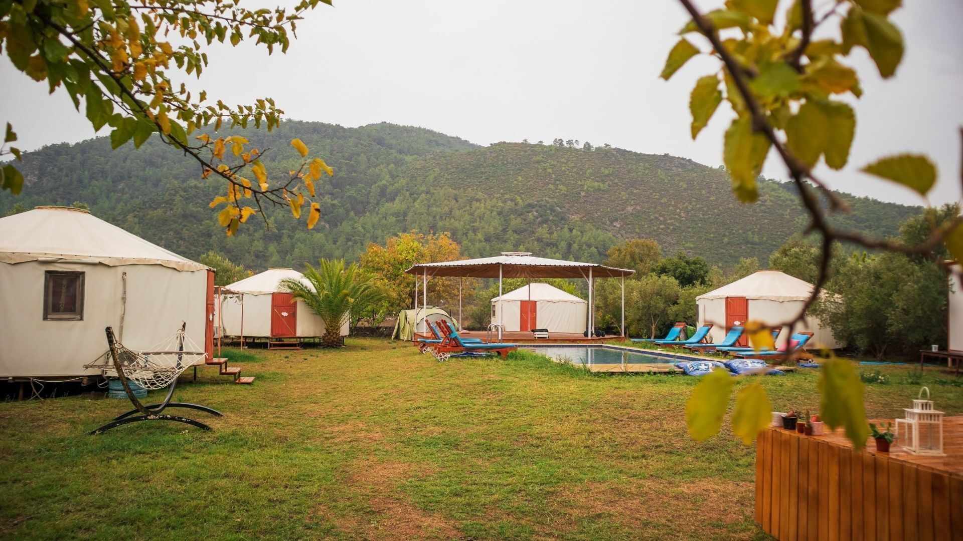 Yurtas con piscina y sillones de descanso, rodeadas de vegetación y colinas.