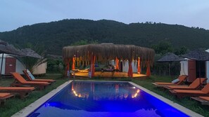 Un área de piscina con sillas de descanso y una estructura de techo de paja.