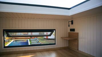 Ein Zimmer mit großem Dachfenster, Holzboden und Blick auf einen Swimmingpool und Gartenmöbel.