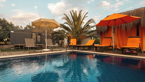 A swimming pool with lounge chairs and umbrellas, surrounded by a wooden deck and a palm tree. - Yol Glamping Hotel Retreat Center (Fethiye)