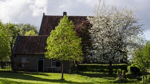 Een bakstenen huis met een schuin dak, omgeven door verzorgde tuinen en bomen.