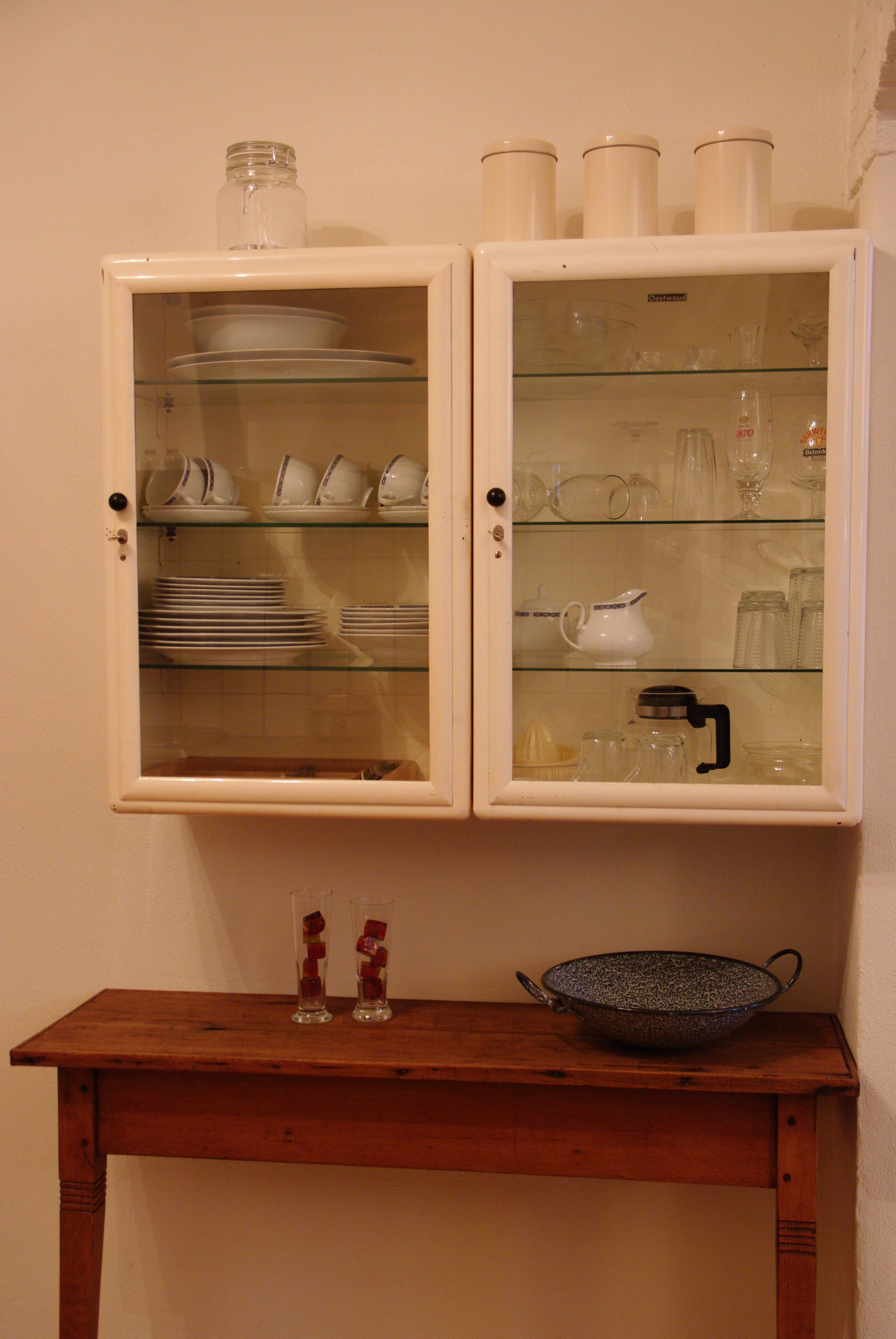 A wooden table with a glass cabinet above it containing various kitchenware.