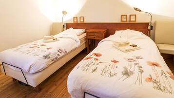 A bedroom with two single beds, wooden headboards, bedside tables, and wall-mounted lamps.