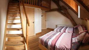 Een houten trap die leidt naar een slaapkamer op een entresol met een schuine kap.