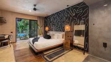 A modern bedroom with a large bed, a desk, and a view of a tropical garden.