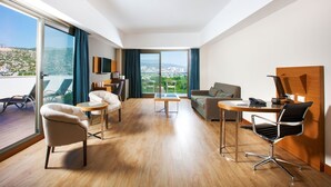 Quarto de hotel moderno com varanda, sofá, escrivaninha e cadeira.