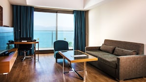 A modern hotel room with a wooden floor, a sofa, a desk, a chair, and a large window with a view of the sea. - Liberty Kusadasi (Kuşadası)