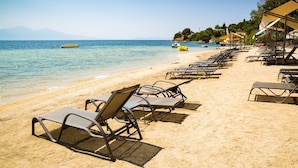 A beach with rows of sun loungers, a clear blue sea, and a boat in the distance. - Liberty Kusadasi (Kuşadası)