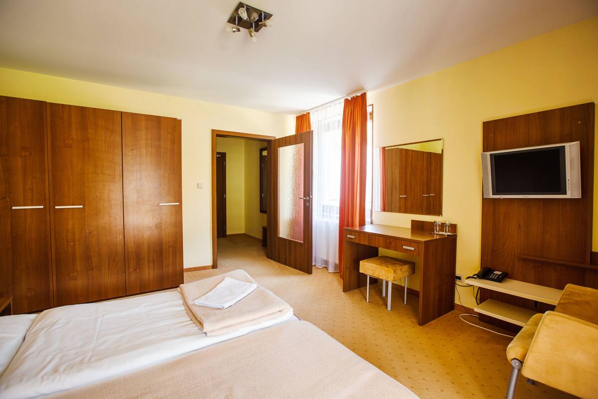 A hotel room with a bed, a desk, a chair, a TV, and a wardrobe.