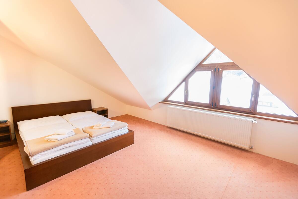 A bedroom with a sloped ceiling, a bed with neatly folded white linens, a bedside table, and a window with a view.