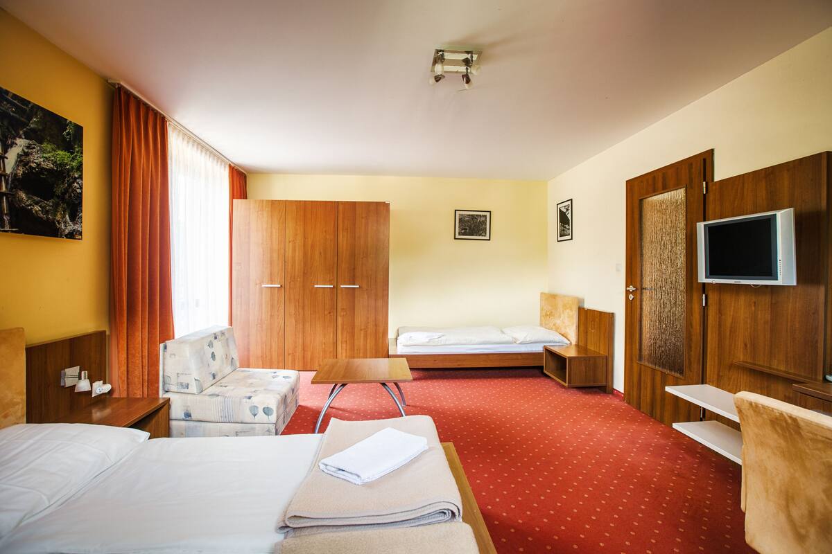 A hotel room with two beds, a sofa, a TV, and a wooden wardrobe.