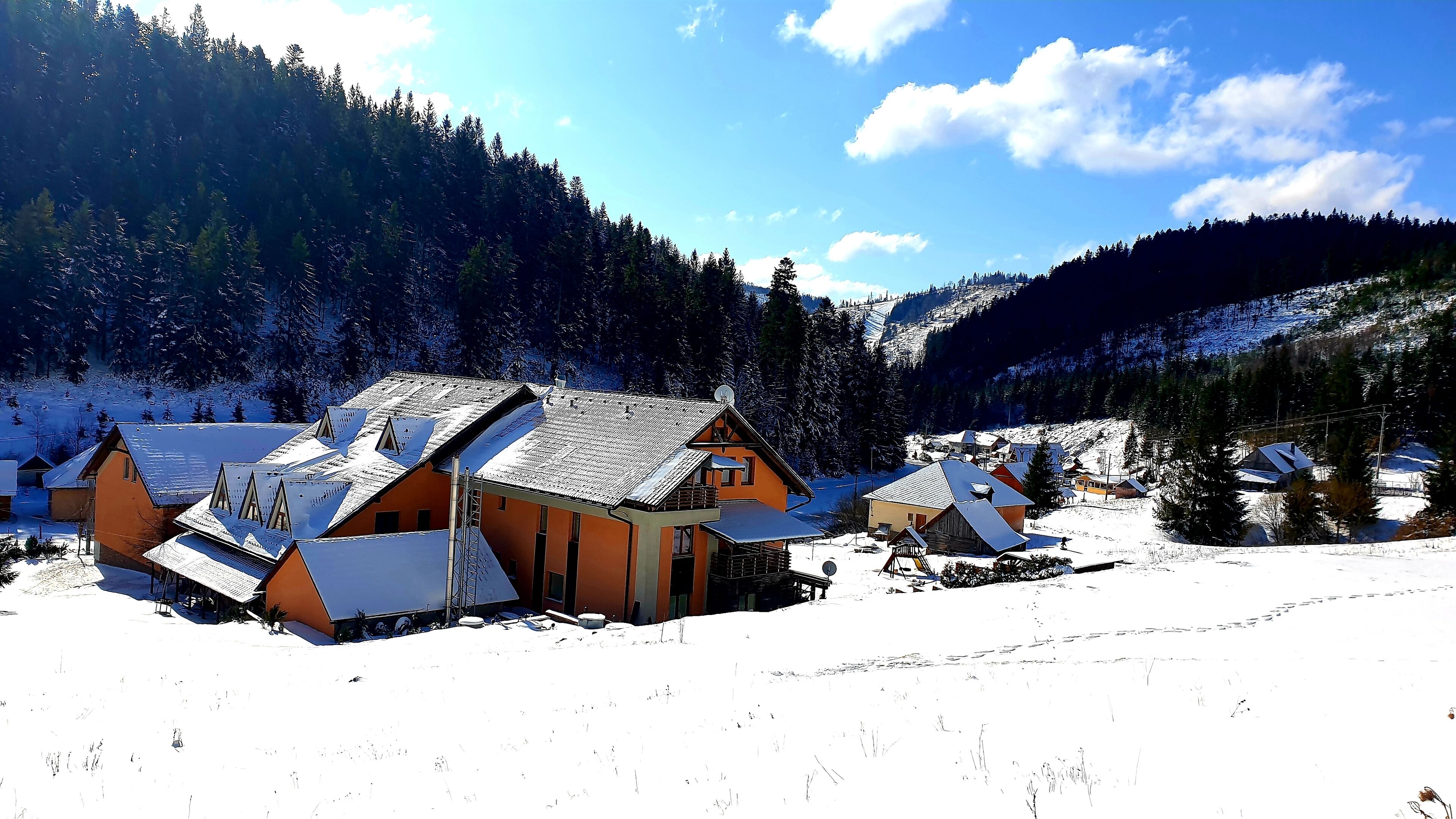 A snow-covered village with traditional wooden houses, a ski lift, and a mountainous backdrop.