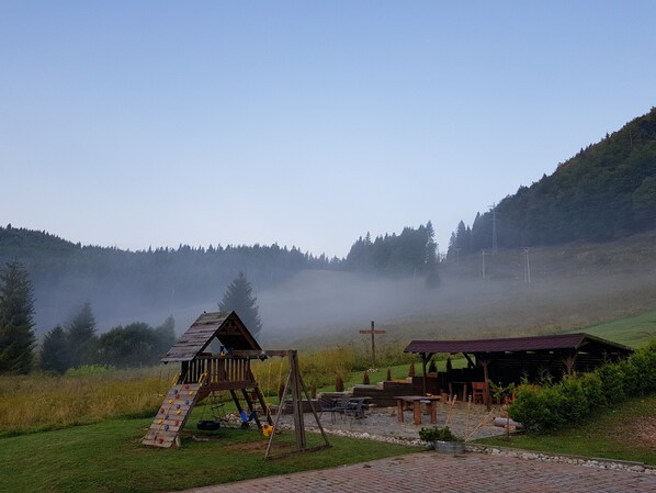 A rustic wooden play structure and a covered picnic area in a misty, forested setting.