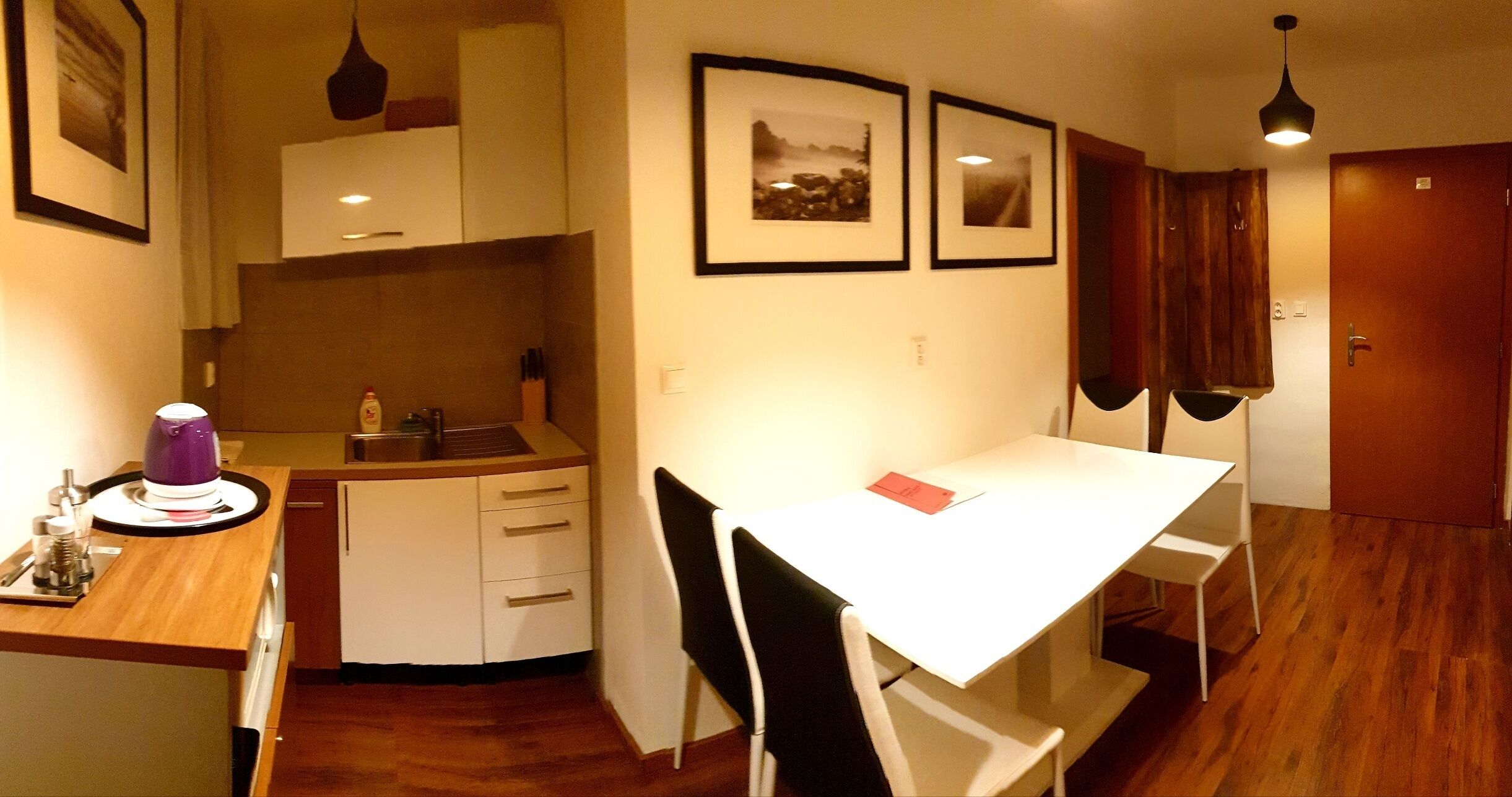 A compact kitchen with a white table and chairs, a coffee maker, and framed pictures on the wall.