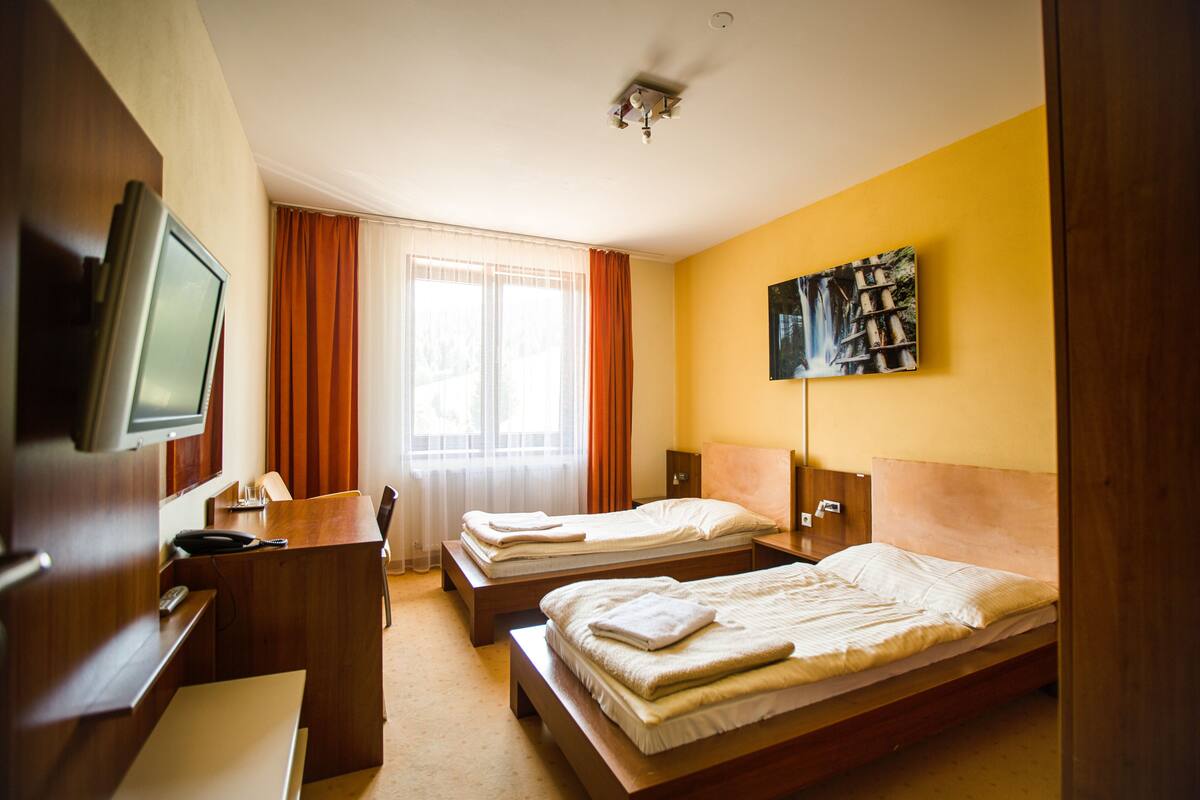 A hotel room with two beds, a desk with a chair, a television, and a bookshelf.