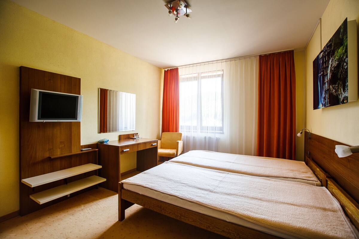 A hotel room with two beds, a desk with a chair, a television, and a window with curtains.