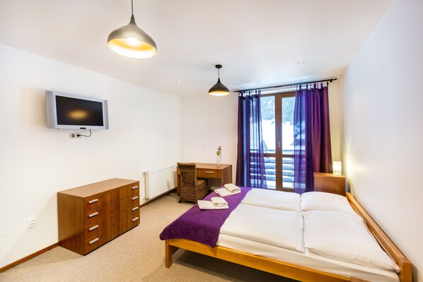 Un dormitorio con cama, cómoda, escritorio, televisor y ventana con cortinas.