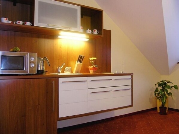 Cocina compacta con microondas, fregadero y muebles blancos.