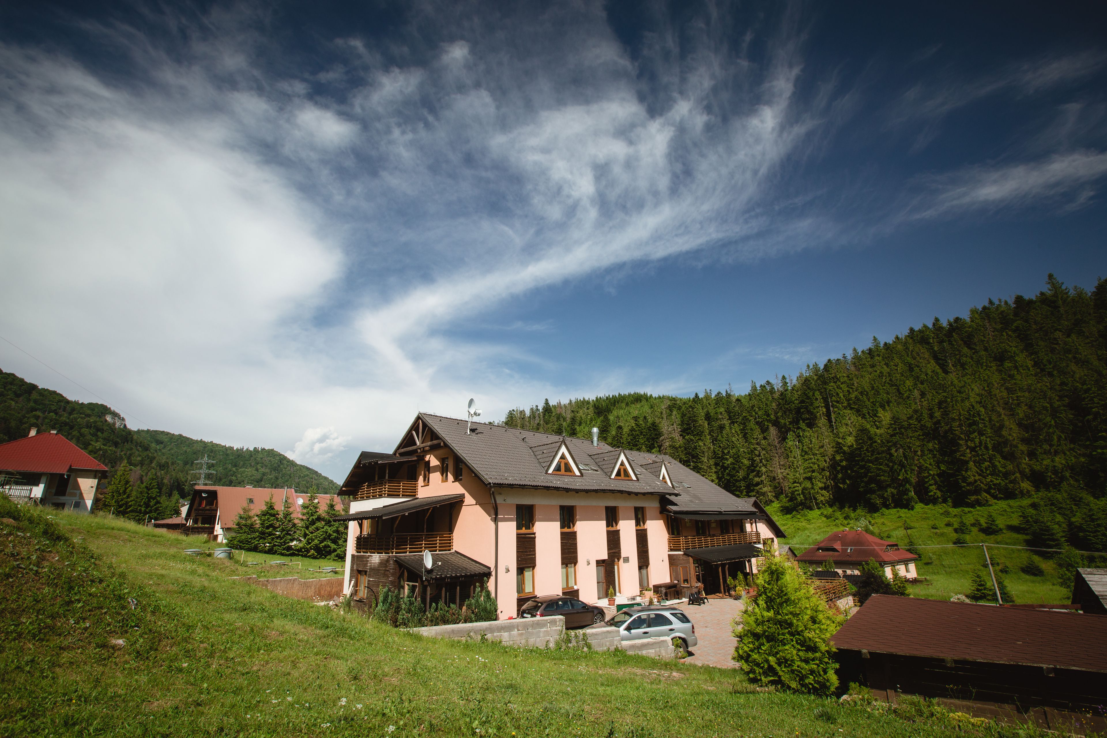 A large building with multiple levels and a sloped roof, surrounded by greenery and a forested hillside.