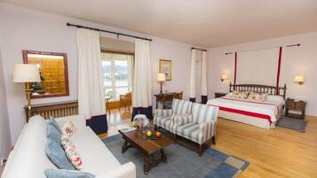 Habitación de hotel con cama, sofá, mesa de centro, lámpara y vistas al exterior.