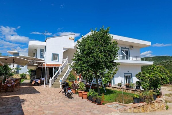 A modern two-story building with a patio area, outdoor seating, and potted plants. - Hotel Chris (Ksamil)