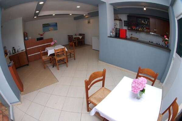 A dining area with a table set for two, a kitchen with a bar, and a small refrigerator. - Hotel Chris (Ksamil)