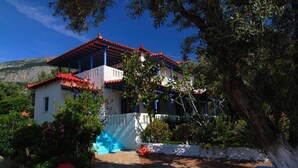 A traditional house with a red-tiled roof, a white exterior, and a stone pathway leading to the entrance. - White Rock Apartments (Samos)