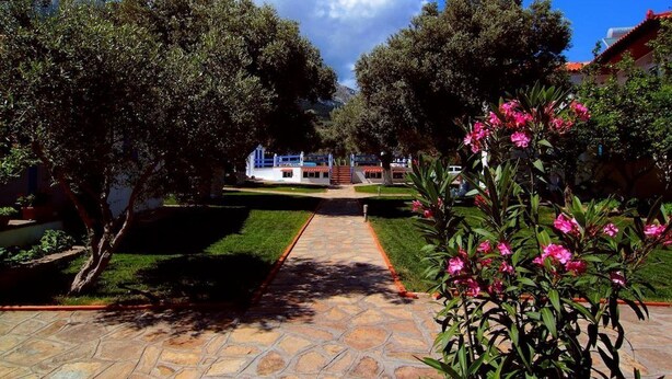 A paved pathway leading to a building with a blue and white structure in the background. - White Rock Apartments (Samos)