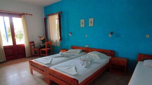A room with two wooden beds, a small table with chairs, a desk, and a window with curtains. - White Rock Apartments (Samos)