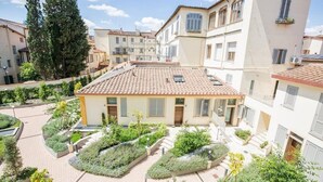 A courtyard with a central building surrounded by greenery and other buildings. - Coco Places (Florence)