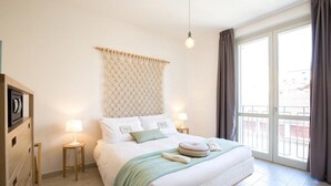 A hotel room with a bed, bedside lamps, a headboard, and a view of the outside through a large window. - Coco Places (Florence)