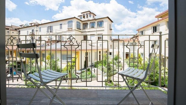 A balcony with two white chairs and a metal railing overlooking a courtyard with buildings and greenery. - Coco Places (Florence)