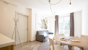 A modern living room with a grey sofa, a round dining table with chairs, a wooden floor, and a large window with curtains. - Coco Places (Florence)