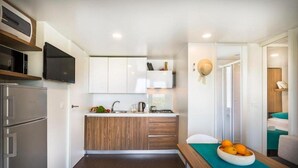 A compact kitchen with white cabinets, a microwave, a stove, and a sink. There's a small countertop with a bowl of fruit. - Aminess Maravea Camping Resort (Novigrad)