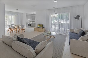 A modern living room with a sofa, a coffee table, and a dining area with chairs. - Elysia Park Luxury Holiday Residences (Paphos)