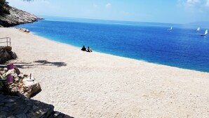 A beach with clear blue water, a few sailboats, and a rocky cliff. - Apartel Park Osejava (Makarska)