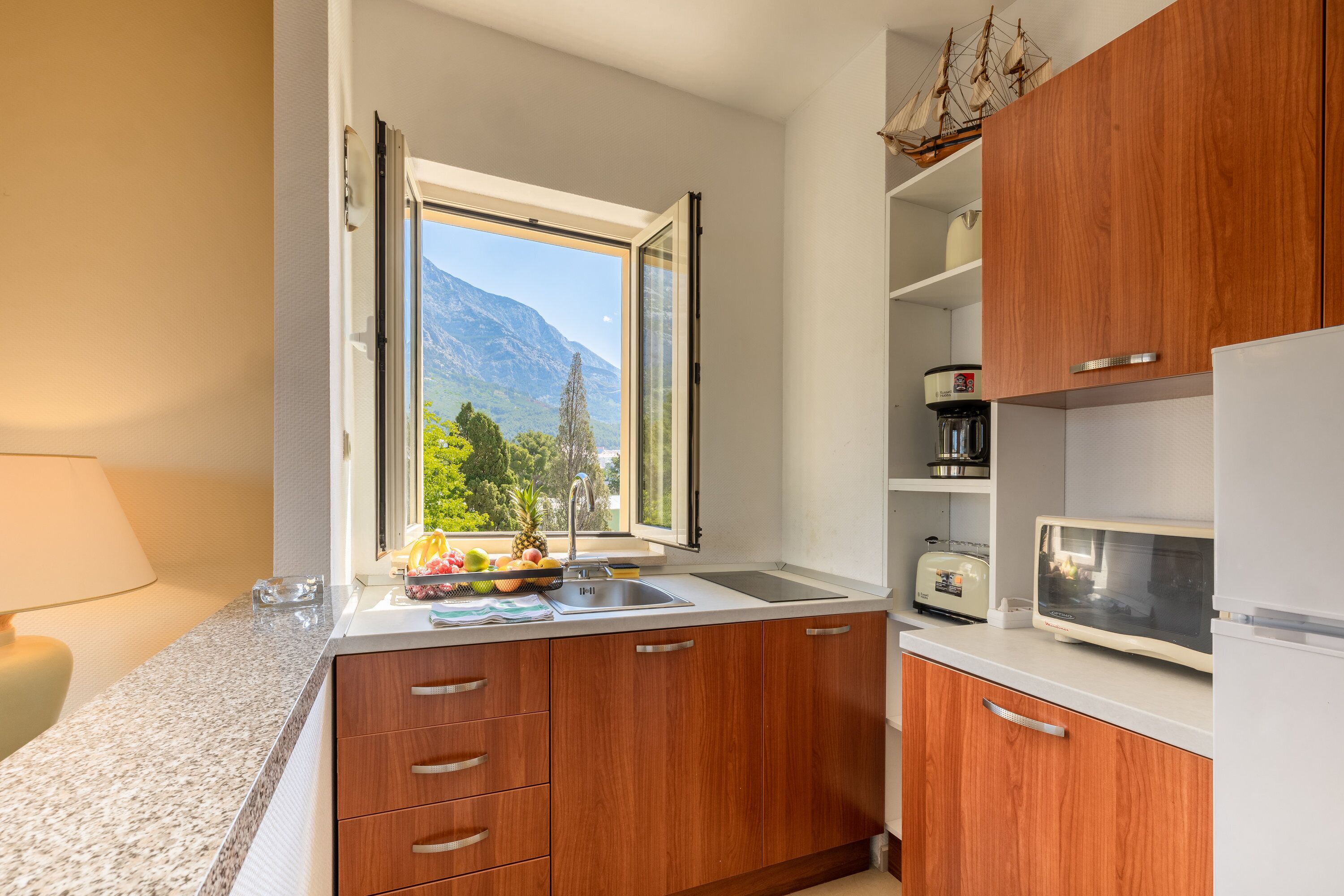 A kitchen with wooden cabinets, a sink, a window with a mountain view, and a microwave.