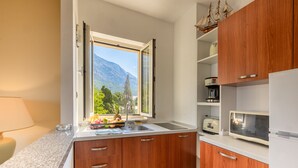 A kitchen with wooden cabinets, a sink, a window with a mountain view, and a microwave. - Apartel Park Osejava (Makarska)