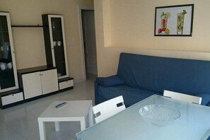 A living room with a blue sofa, a glass coffee table, a white TV stand with cabinets, and a framed picture on the wall. - Residencial Las Calas (Torrevieja)