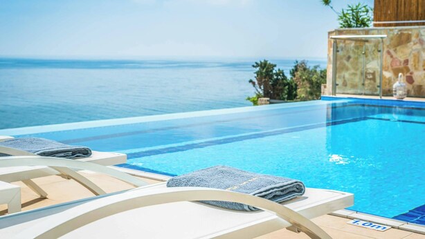 An infinity pool with clear blue water, lounge chairs, and a view of the ocean. - Villa Azure (Kefalonia)