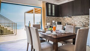 A modern kitchen with dark cabinets, a tiled backsplash, and a dining area with a table set for breakfast. - Villa Azure (Kefalonia)
