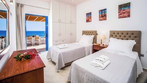 A hotel room with two beds, a wooden desk, a view of the sea, and artwork on the wall. - Villa Azure (Kefalonia)
