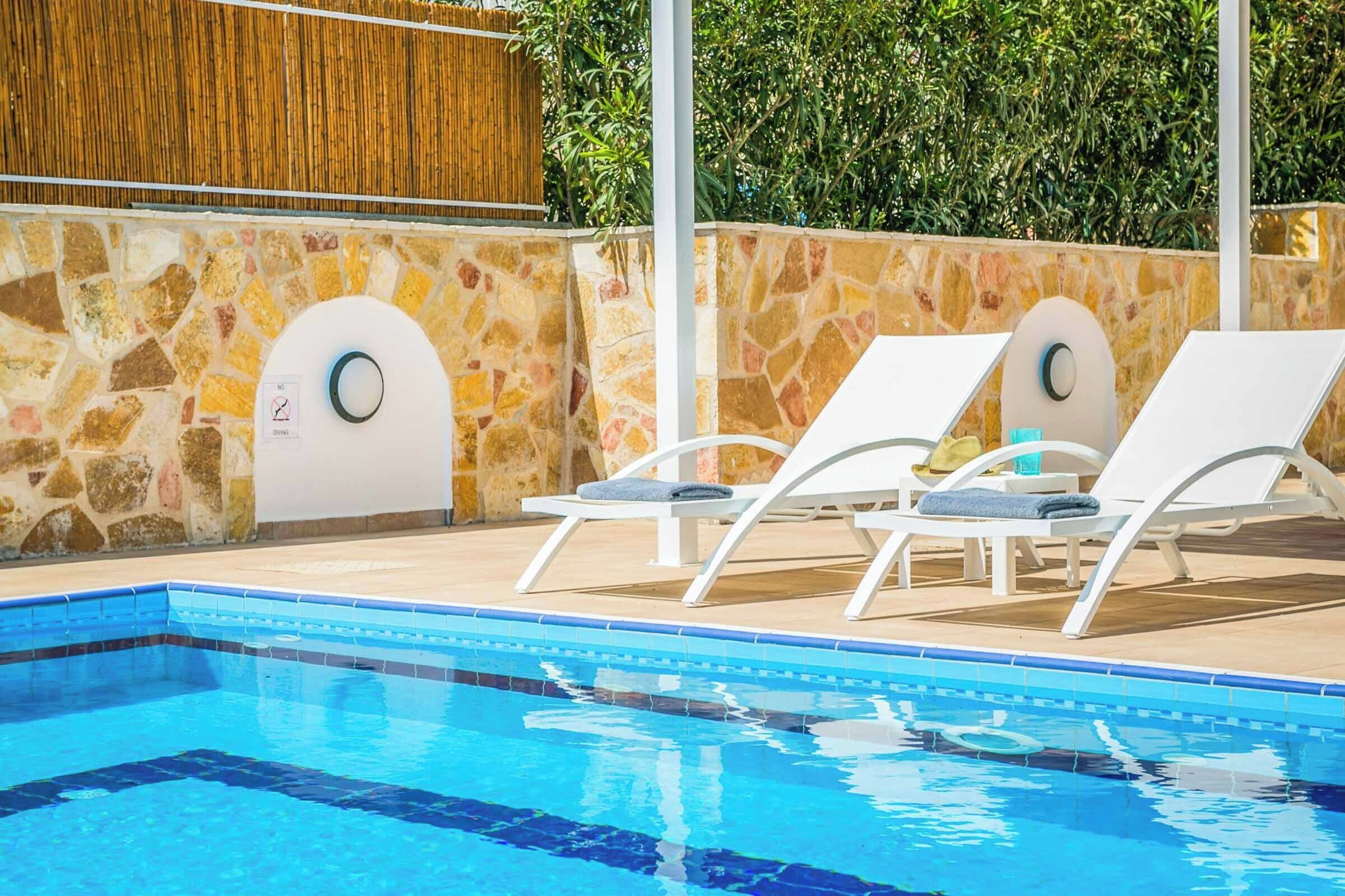 Piscina com duas espreguiçadeiras e um muro de pedra.