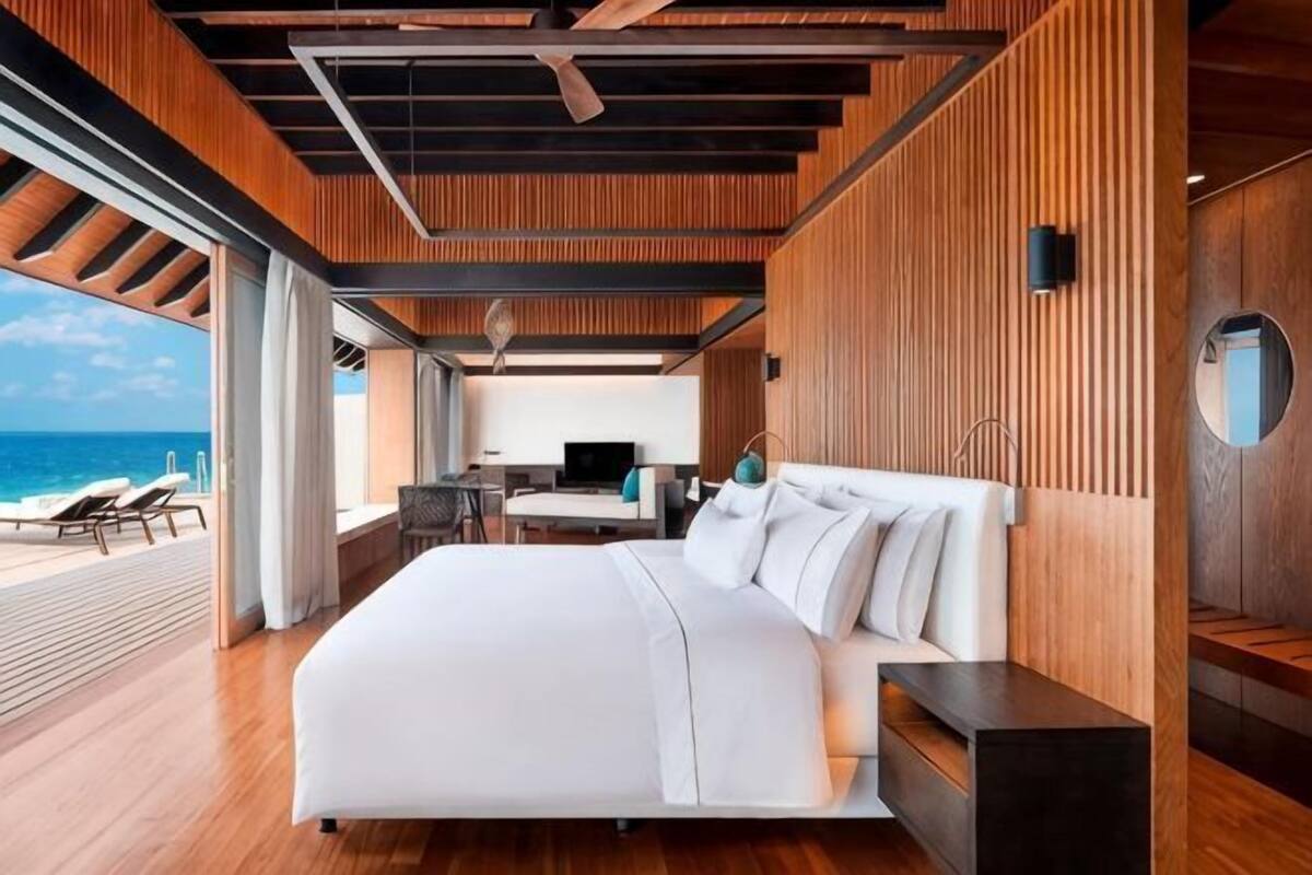 A modern bedroom with a large bed, wooden paneling, a desk, and a view of the ocean.