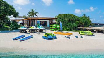 A beach with a building, clear turquoise water, and various watercraft.