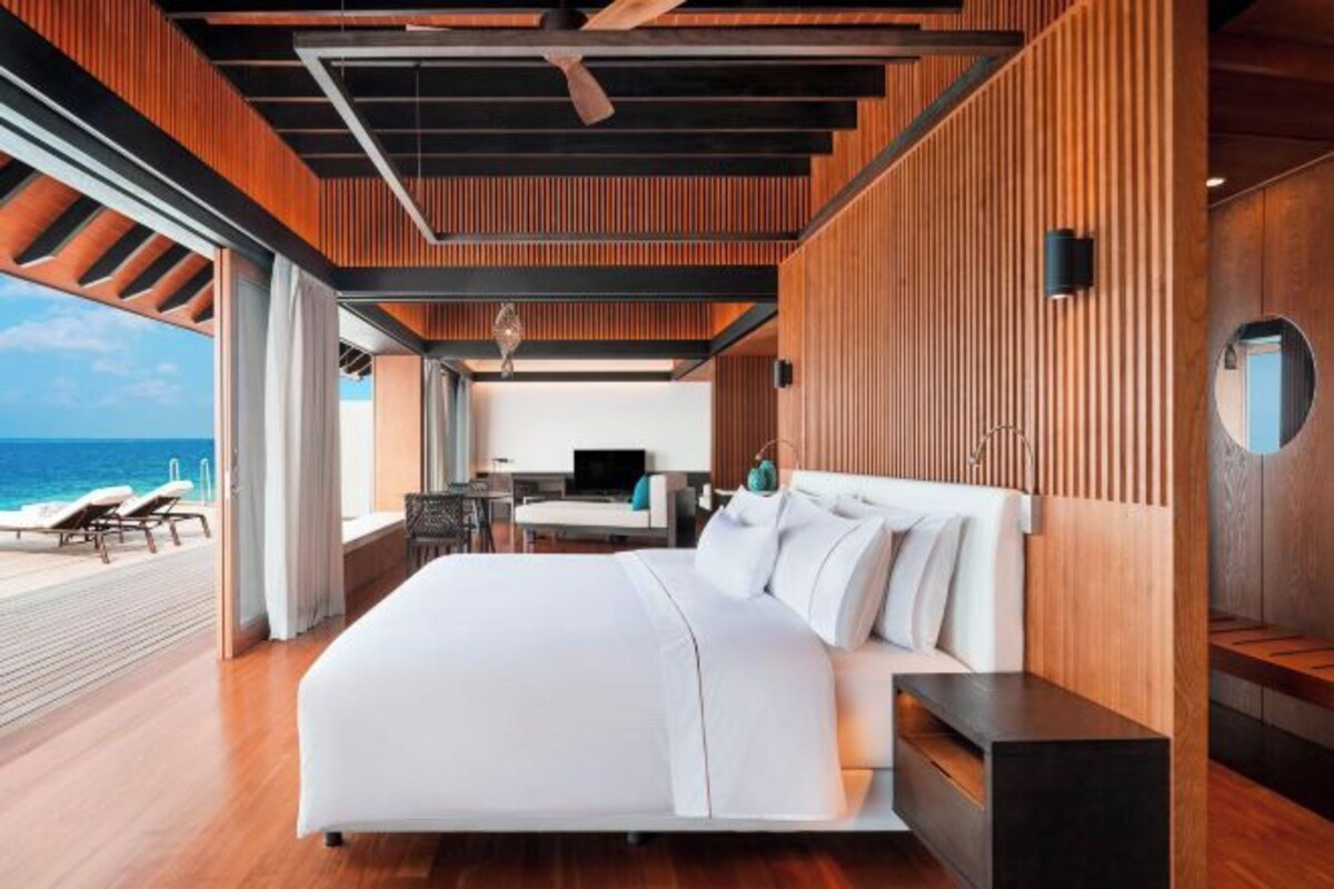 A modern bedroom with a large bed, wooden paneling, a TV, and a view of the ocean.
