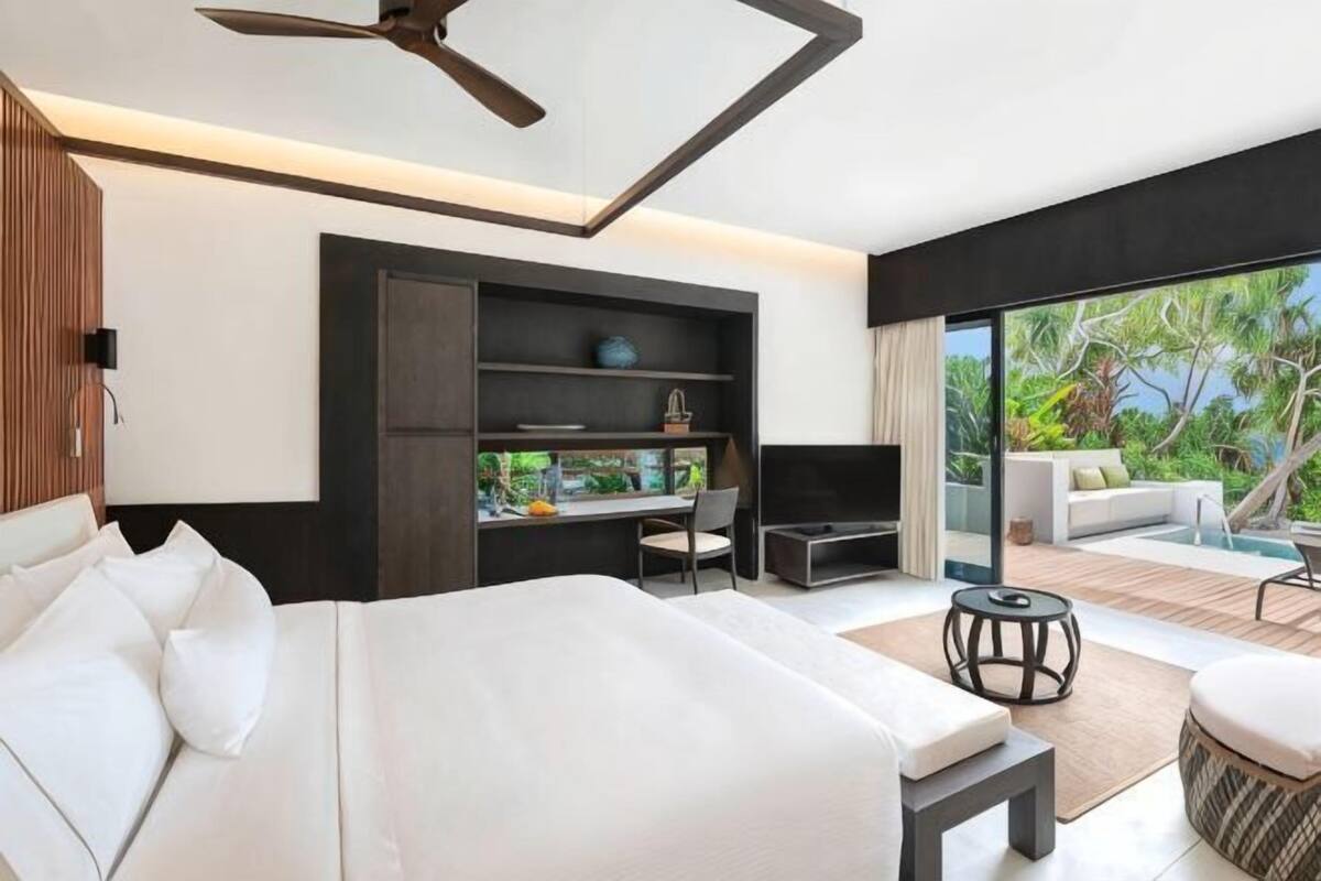 A modern hotel room with a bed, desk, and seating area with a view of the outdoors.