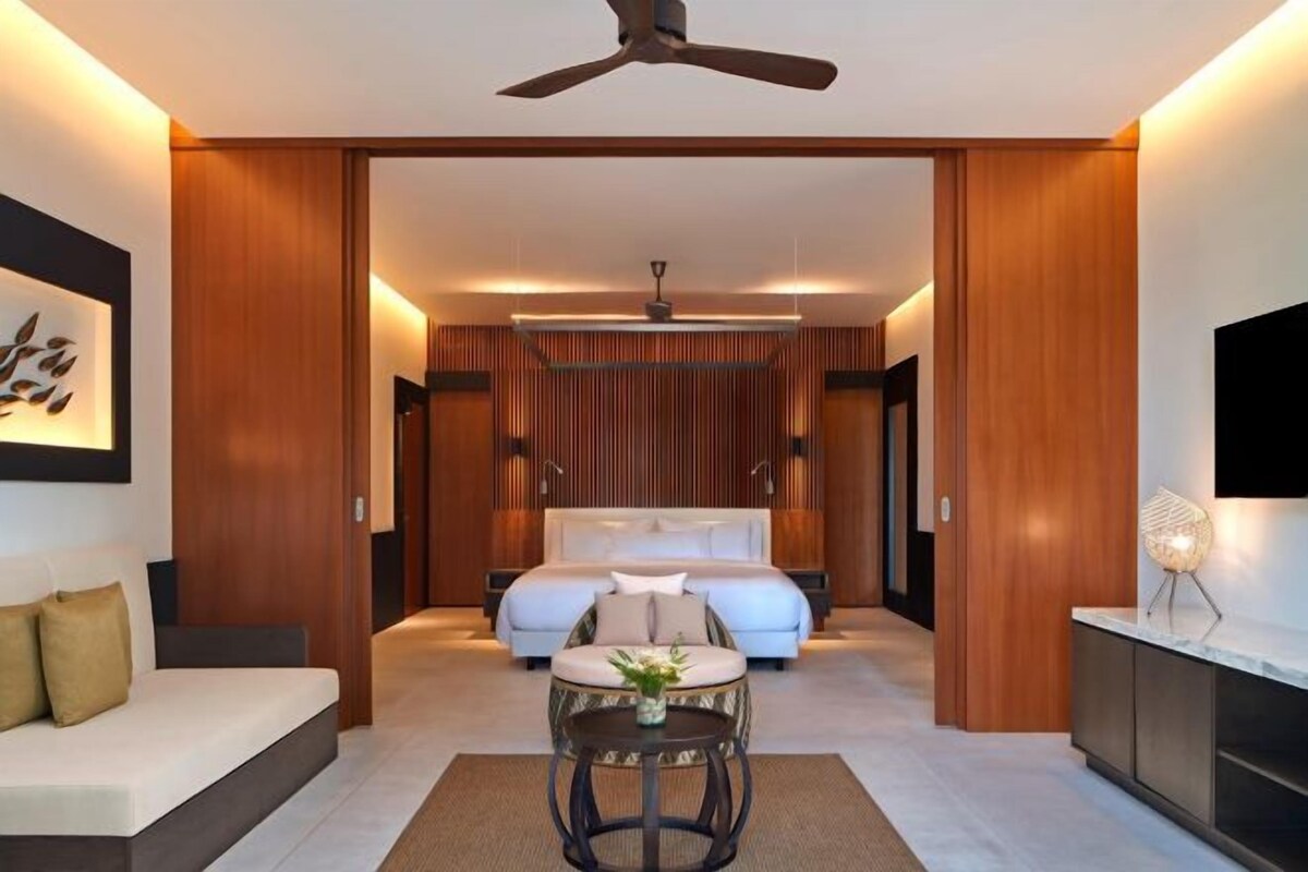 A modern hotel room with a large bed, a seating area with a table, and a TV on the wall.